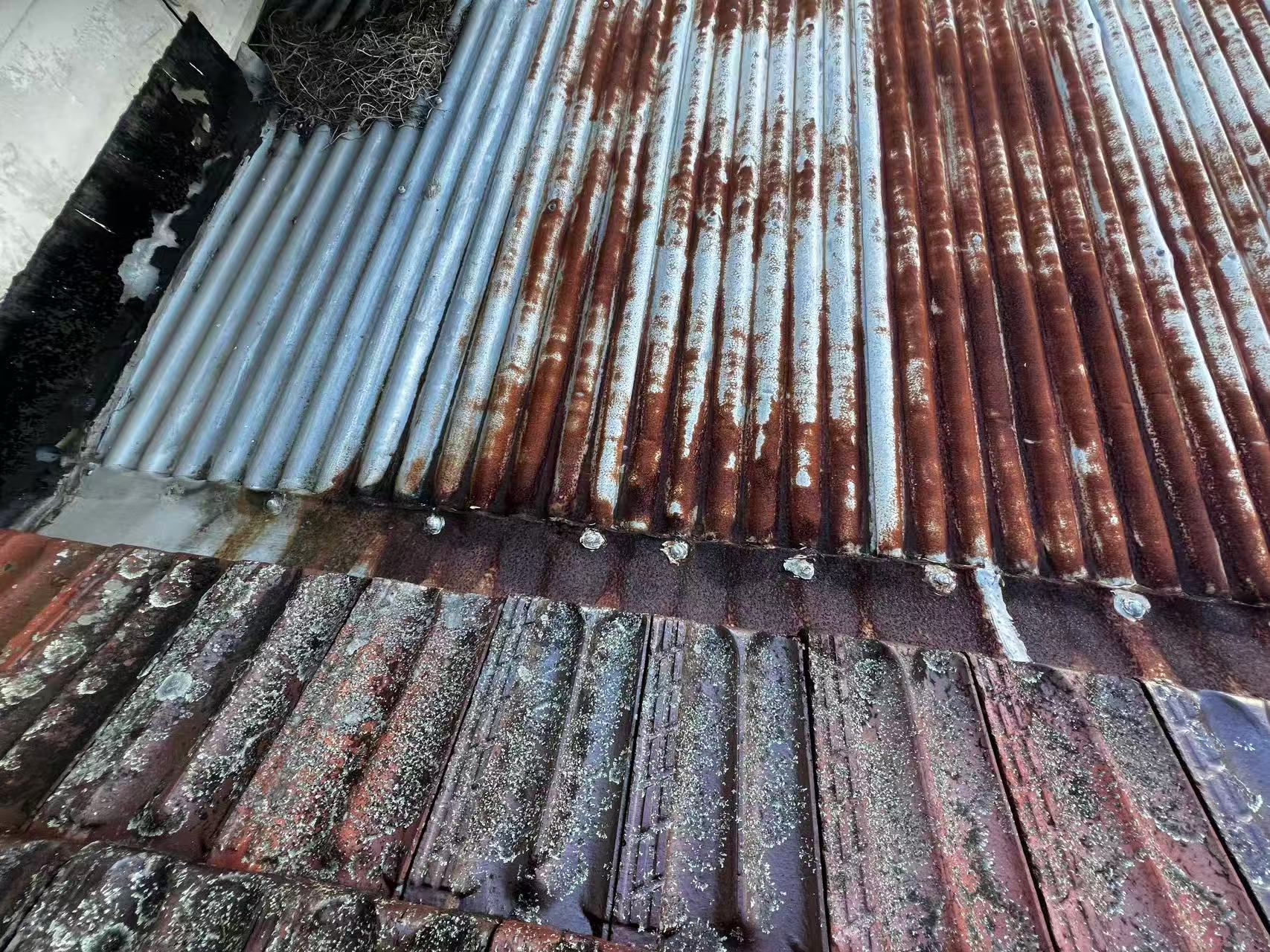 Corroded corrugated metal sheets beside the tiled roof junction
