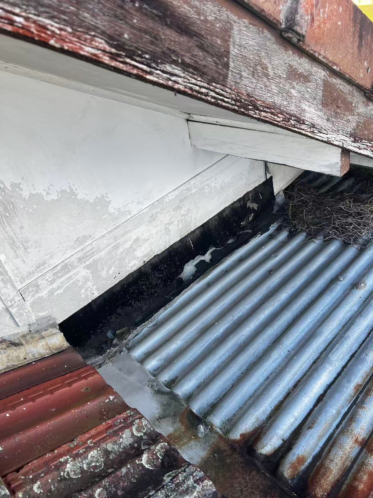 Roof-to-wall junction with weathered timber and debris beside the metal sheets